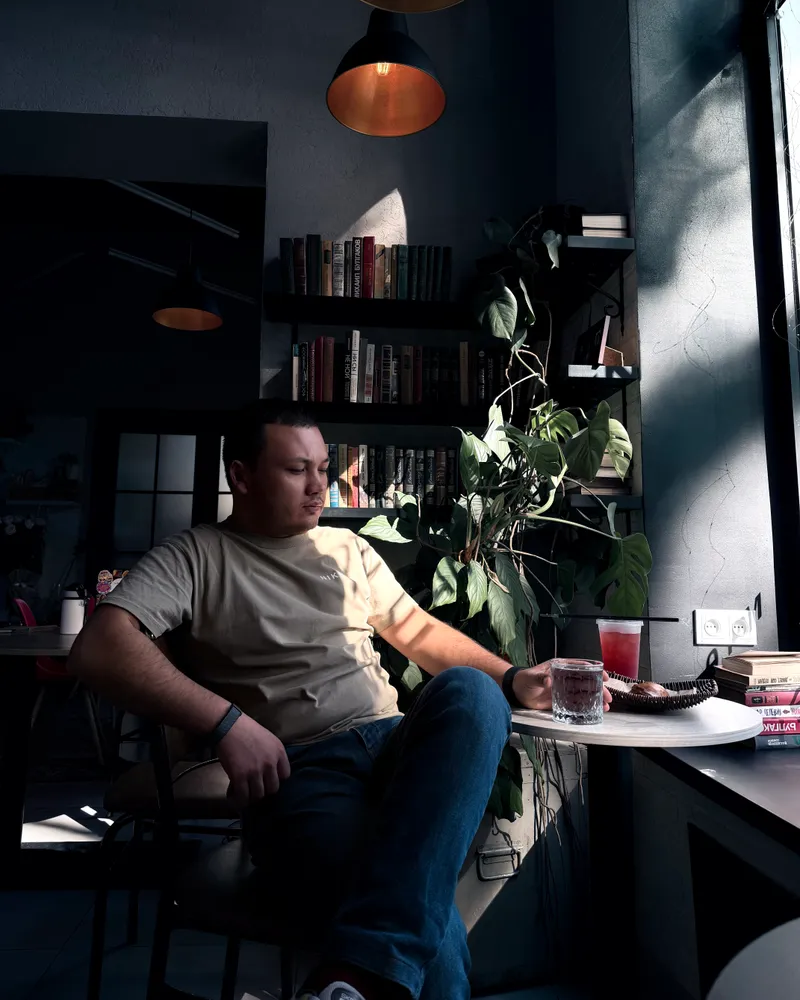 Jamik sitting by a bookshelf in a café in Tashkent